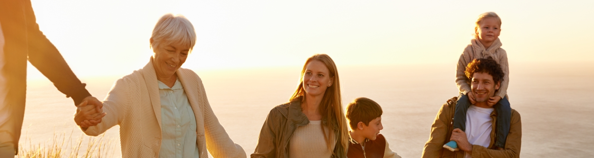 A multi-generational family walking up a grassy hill together at sunset 